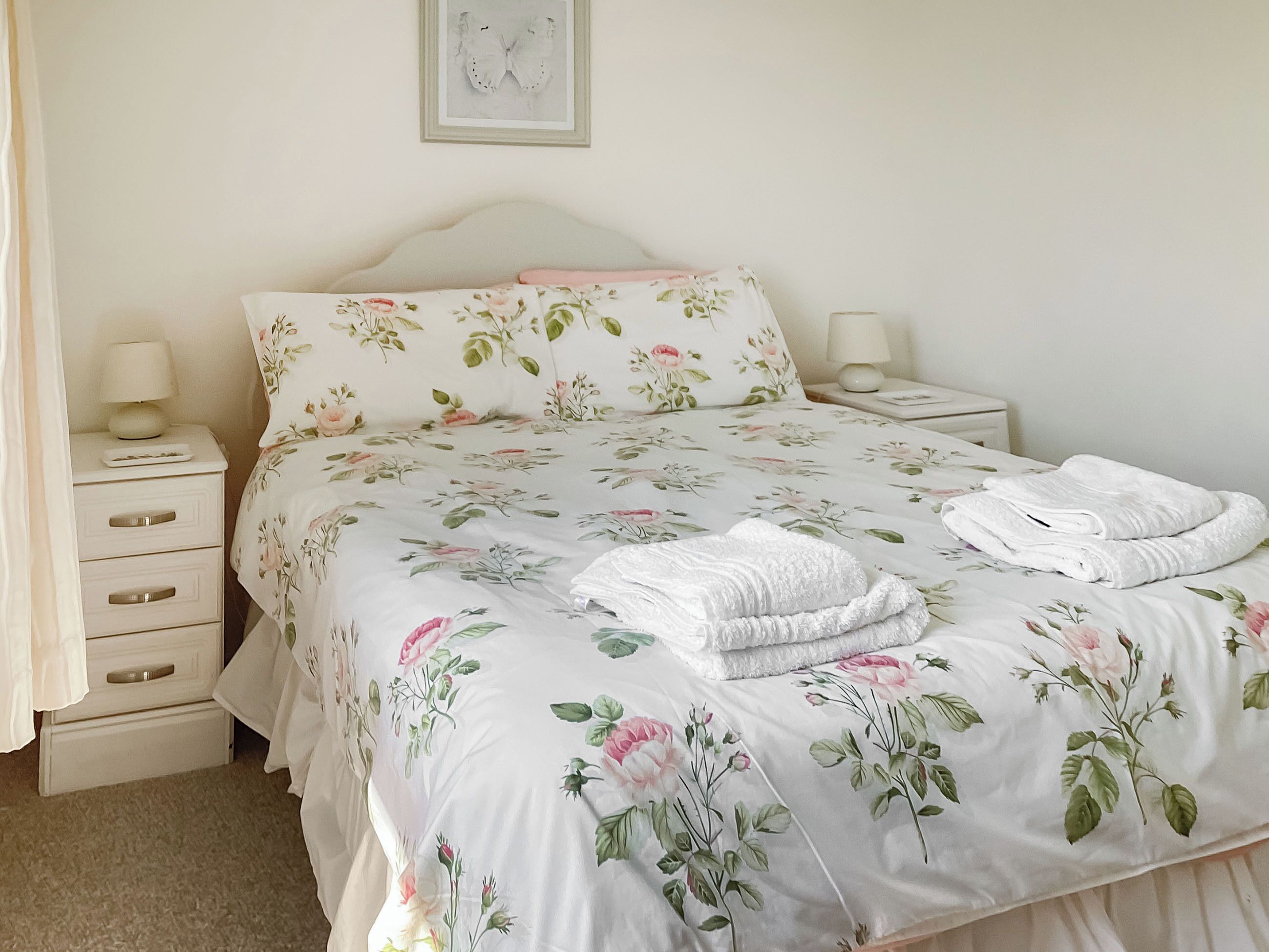 Una cama bien hecha con ropa de cama floral, dos lámparas de noche y una mesita de noche con lámpara.