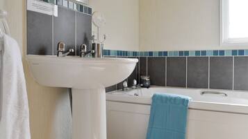 A bathroom with a white sink, a bathtub, and a blue towel hanging on the wall.