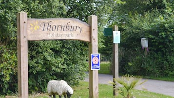 Señal de madera del Thornbury Holiday Park con una oveja pastando cerca.