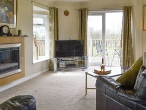 A living room with a fireplace, television, and a balcony with outdoor furniture. - 2 bedroom accommodation in Woodacott, near Holsworthy (Woodacott, near Holsworthy)