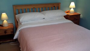En snyggt bäddad säng med ett rosa överkast, två sänglampor och en sänggavel i trä.