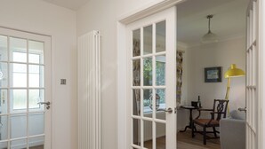Una habitación con un radiador blanco, una puerta con paneles de vidrio, suelo de madera y un comedor con mesa y sillas.