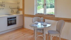 A kitchen with a built-in oven, a dining table with two chairs, and a window with a view of greenery.