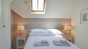 A bedroom with a large bed, two bedside tables with lamps, a skylight, and a wooden headboard.