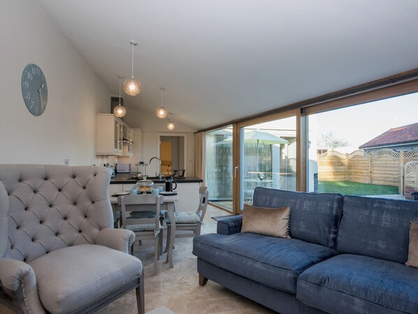 A modern living room with a sofa, a chair, a dining table, and a kitchen area with a sink and cabinets.