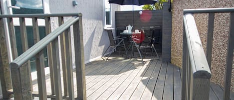 Un terrazzo in legno con tavolo e sedie, un ombrellino e vista su un edificio.