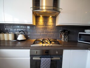 Une cuisine moderne équipée d’une cuisinière à gaz, d’appareils électroménagers en acier inoxydable et d’une hotte en verre.