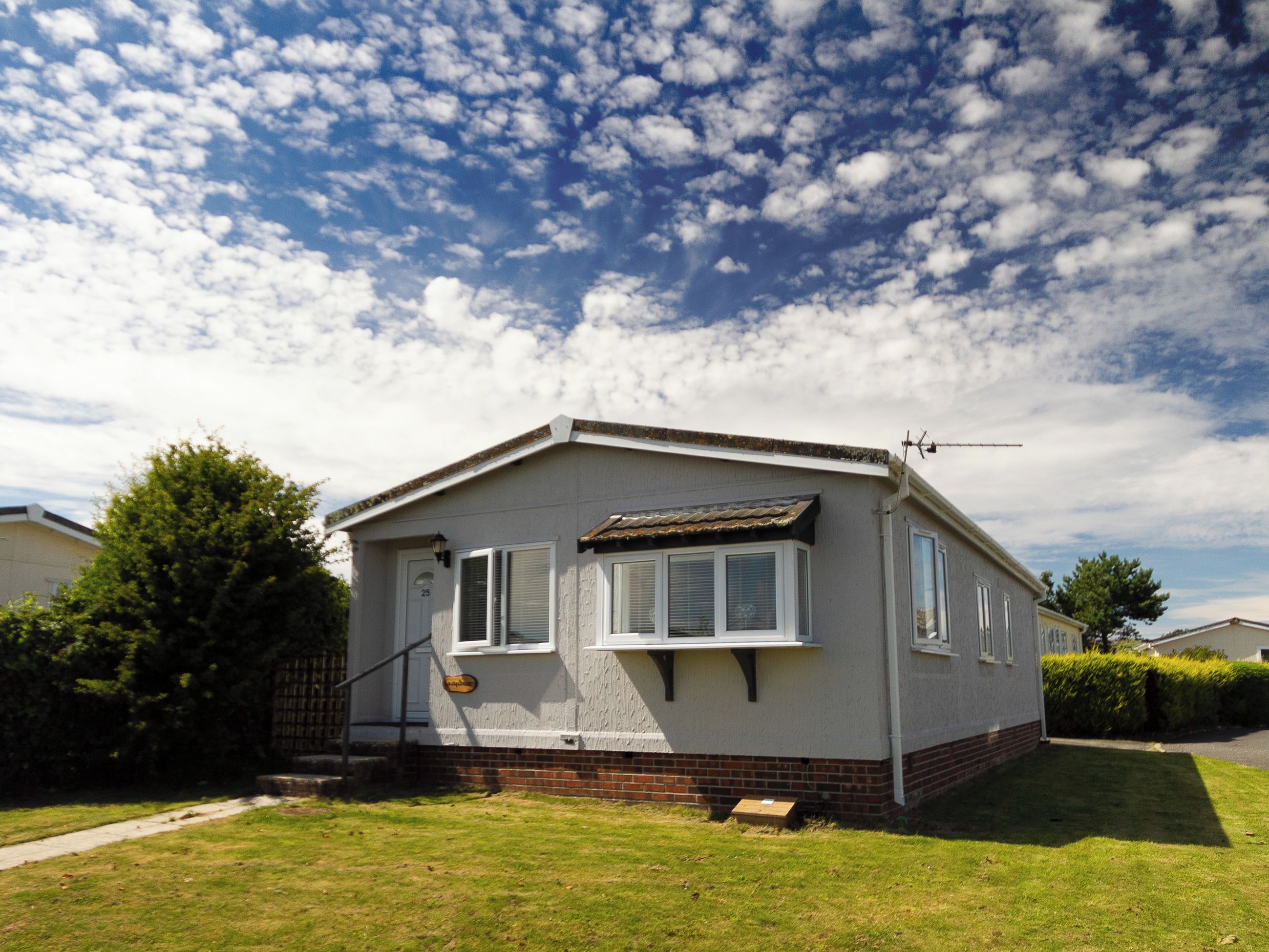 A single-story mobile home with a front porch, a small front yard, and a clear sky with clouds.