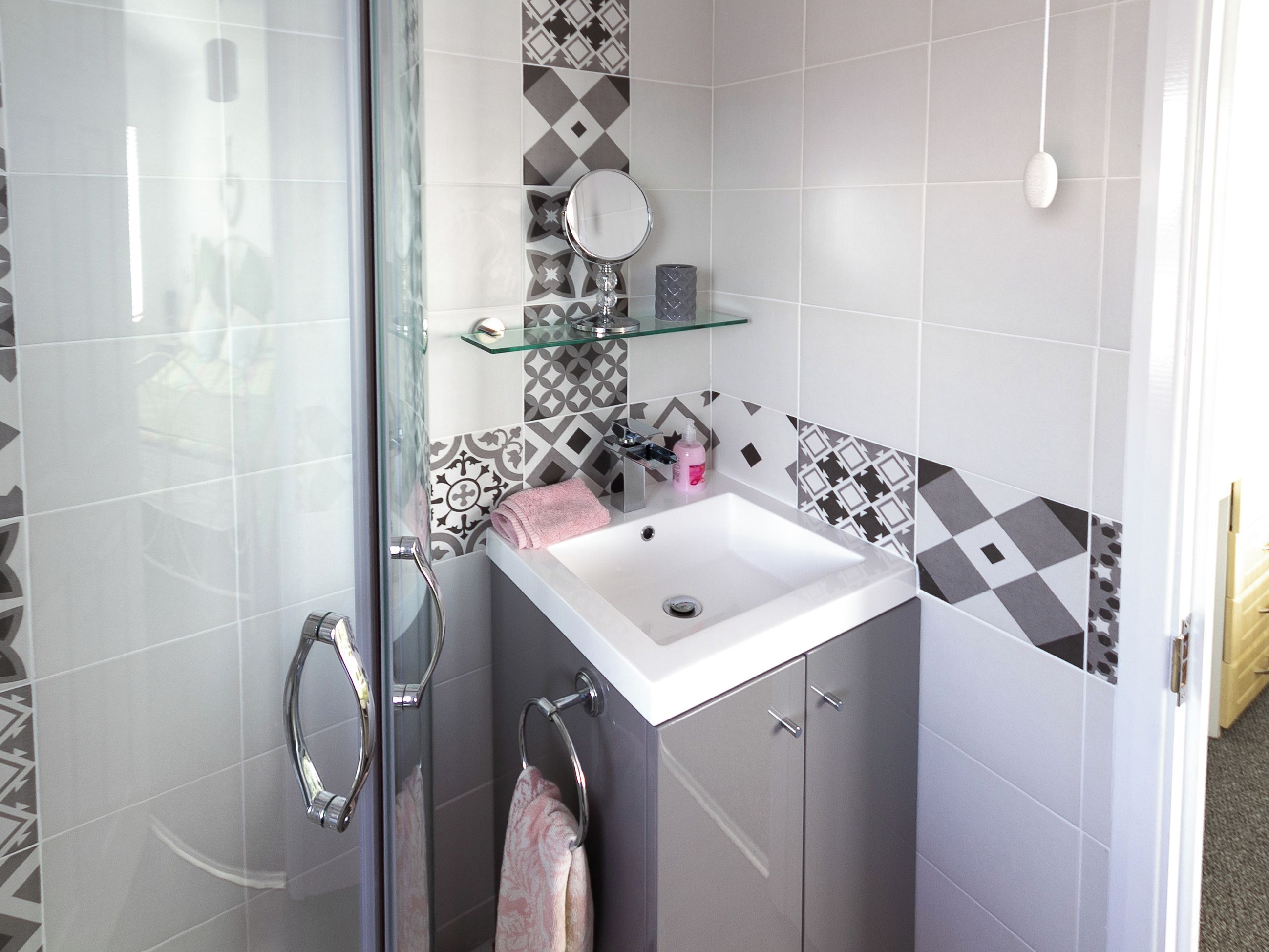 A bathroom with a glass shower enclosure, a white sink, and patterned tiles.