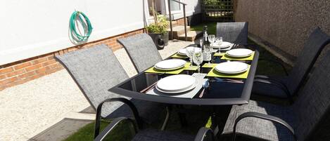 An outdoor dining area with a table set for four, surrounded by chairs, in a residential setting.