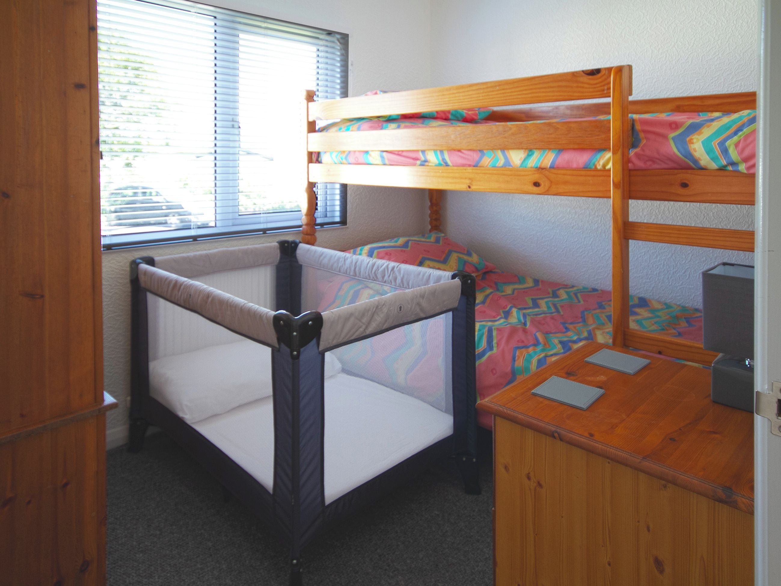 A bunk bed with a lower bunk and a mattress with a colorful geometric pattern. There is a small desk with a chair and a computer.