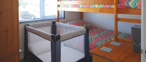 A bunk bed with a lower bunk and a mattress with a colorful geometric pattern. There is a small desk with a chair and a computer.