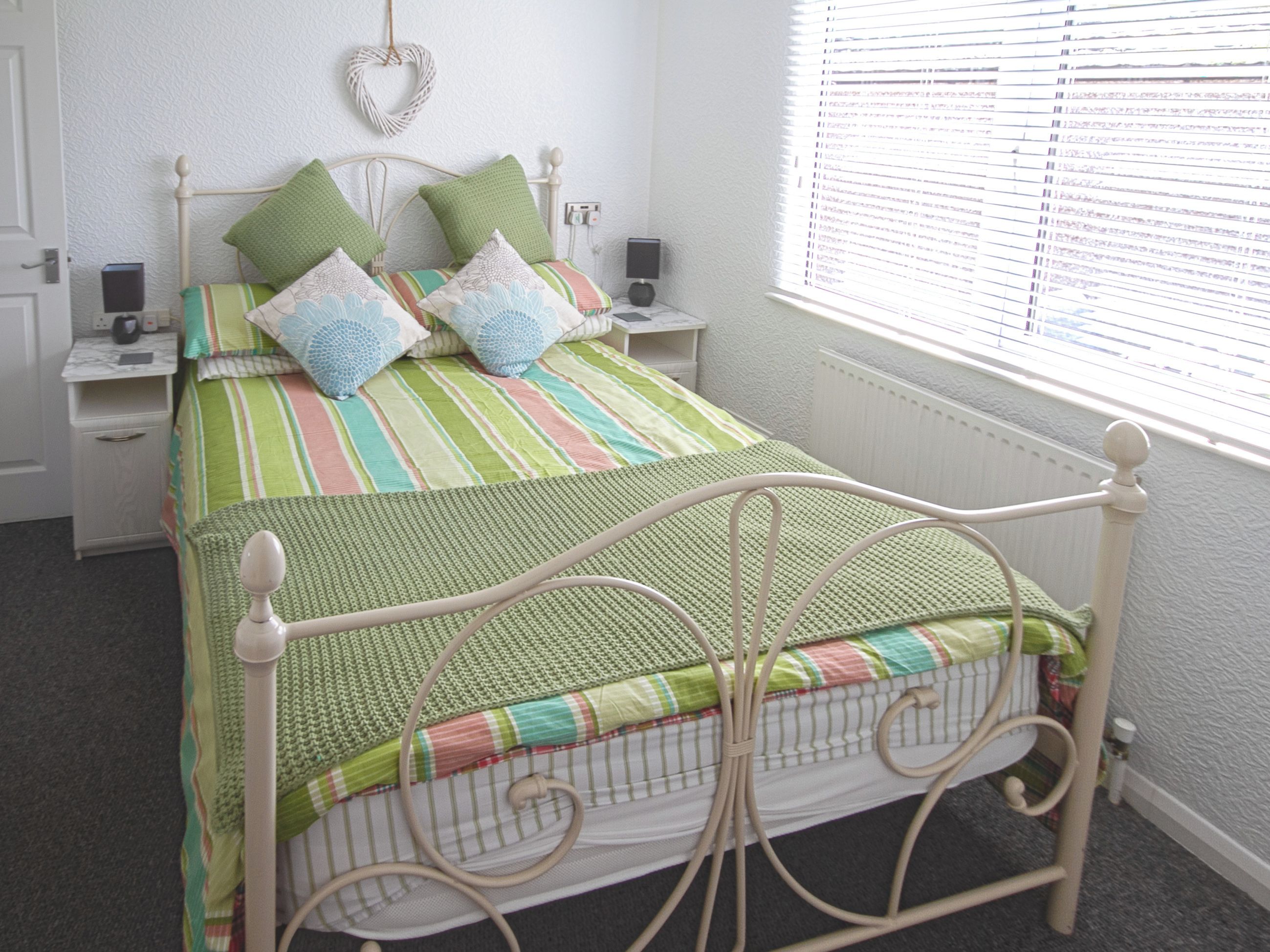 A neatly made bed with a green and striped bedspread, two pillows, and a headboard.