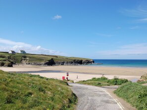 A coastal road leading to a beach with houses on a grassy hill.