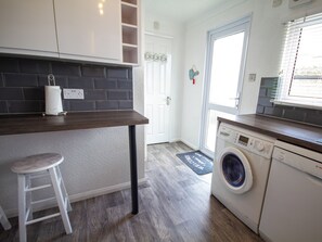 Une cuisine compacte dotée d’un lave-linge encastré, d’un tabouret de bar blanc et d’un plan de travail en bois.