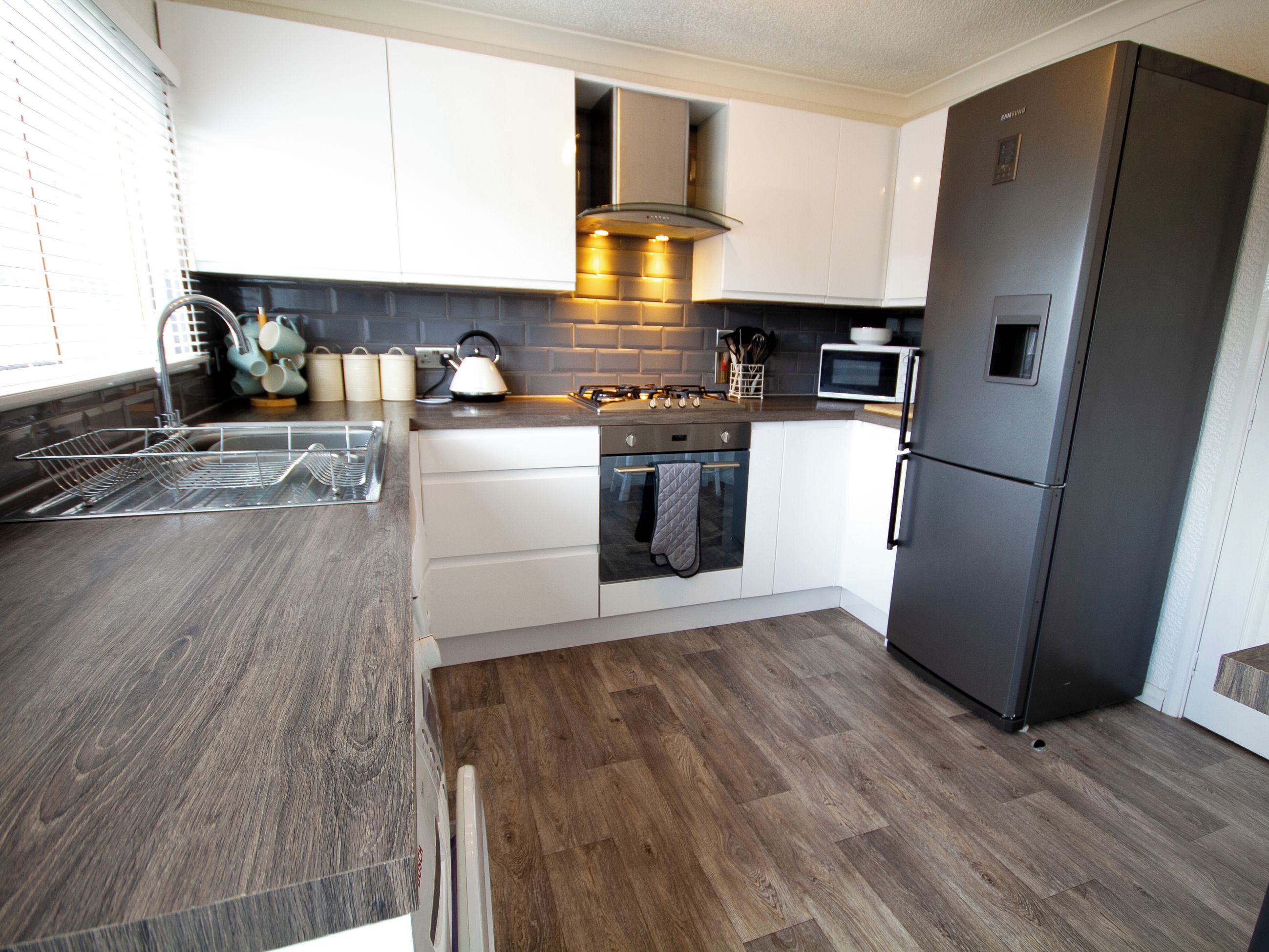 A modern kitchen with white cabinets, a stainless steel refrigerator, a built-in oven, and a microwave.