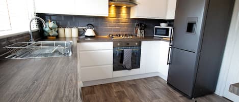 A modern kitchen with white cabinets, a stainless steel refrigerator, a built-in oven, and a microwave.