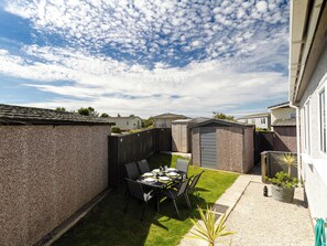 A backyard with a dining table set for four, surrounded by chairs, a small garden, and a wooden fence.
