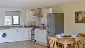 A modern kitchen with a built-in washer, oven, and refrigerator. There is a dining table with chairs and a painting on the wall.