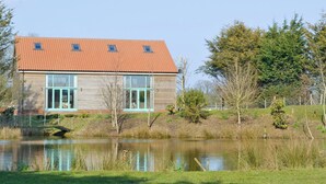 A two-story house with a red-tiled roof, large windows, and a pond in the foreground.