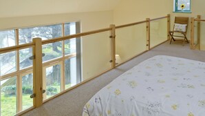 A bedroom with a large window, a wooden railing, a bed with floral bedding, and a chair with a cushion.