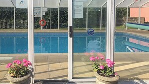 Uma área de piscina com entrada por porta de vidro, um salva-vidas e dois vasos de flores.
