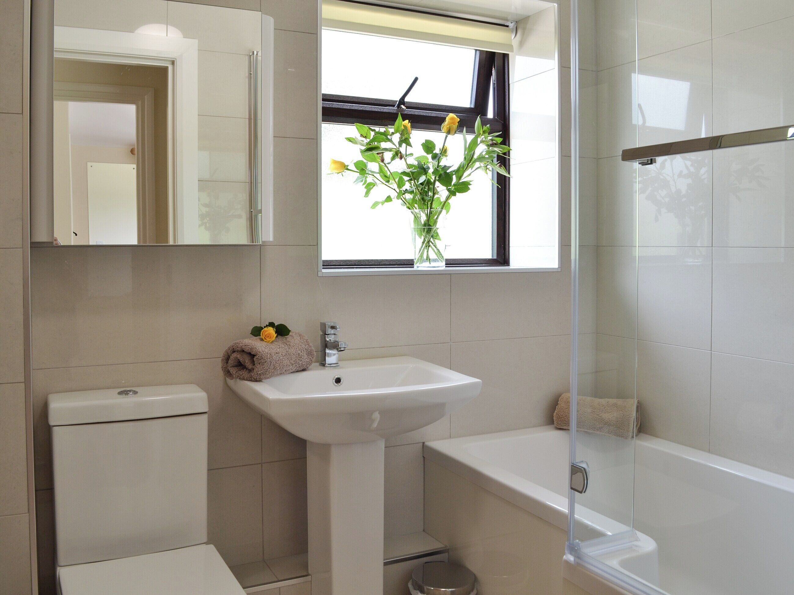 A bathroom with a toilet, sink, and bathtub. There is a window with a plant and a towel on the sink.