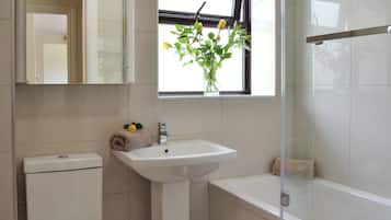 A bathroom with a toilet, sink, and bathtub. There is a window with a plant and a towel on the sink.