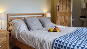 A neatly made bed with pillows, a bedside table with a lamp, and a breakfast tray with croissants and juice. - 2 bedroom accommodation in Wadhurst, near Tunbridge Wells (Wadhurst, near Tunbridge Wells)