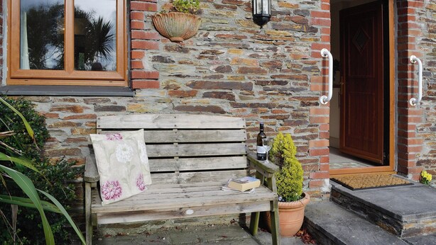 A stone building with a wooden bench outside, a potted plant, and a door with a handle. - A well-appointed, single storey cottage, close to the pretty village of St. (St Merryn, near Padstow)