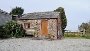 A stone cottage with a wooden door, a bench, and potted plants in front. - A well-appointed, single storey cottage, close to the pretty village of St. (St Merryn, near Padstow)