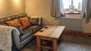 A cozy living room with a leather sofa, a wooden coffee table, and a window with patterned curtains. - A well-appointed, single storey cottage, close to the pretty village of St. (St Merryn, near Padstow)