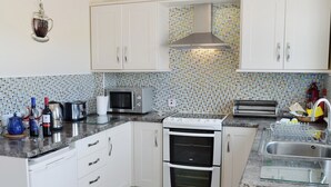 Een moderne keuken met witte kasten, een RVS magnetron, een dubbele oven en een betegelde spatwand.