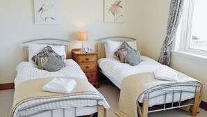Een kamer met twee eenpersoonsbedden, nachtkastje met lamp en raam voorzien van gordijnen.