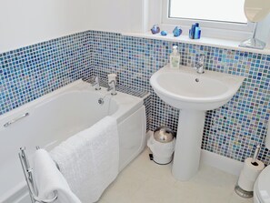 A bathroom with a bathtub, a white sink, and blue mosaic tiles.