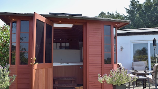 Una cabaña de madera con puerta corredera, un jacuzzi y un patio con mobiliario exterior.