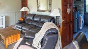 Una sala de estar con un sofá de cuero, dos mesas auxiliares con lámparas, un mueble de madera y un espejo en la pared.