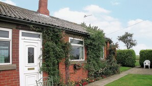 A brick house with ivy, a white door, and a window. There is a white chair and a round table outside. - 1 bedroom accommodation in Fraisthorpe, near Bridlington (Fraisthorpe, near Bridlington)