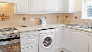 Een keuken met witte kastjes, een fornuis, een wasmachine en een waterkoker.