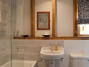 Un baño con cabina de ducha de vidrio, un lavamanos blanco con espejo y un inodoro.