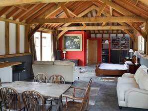 Una habitación rústica con techo de madera, una cama, un sofá, una mesa de comedor con sillas y una pared roja con un cuadro enmarcado.