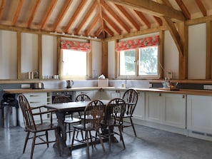 Una cocina con vigas de madera, una mesa de comedor con sillas, un ventanal con un toldo rojo y un lavamanos.