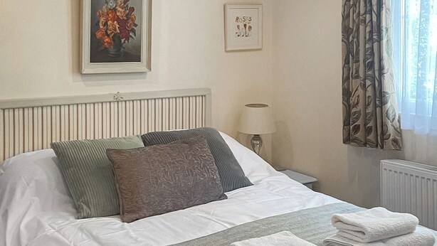 Ein ordentlich bezogenes Bett mit Kissen, einer Nachttischlampe und einem gerahmten Bild an der Wand.