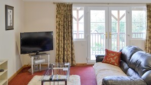 Ein Wohnzimmer mit Fernseher, Ledersofa und Glastisch.