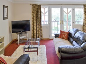 A living room with a TV, leather sofa, and a glass coffee table. - 1 bedroom accommodation in Polperro, near Looe (Polperro, near Looe)