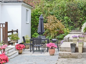 An outdoor patio with a table and chairs, surrounded by potted plants and a garden.