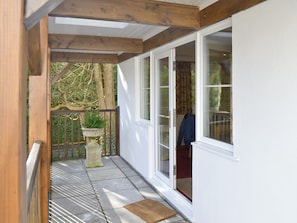 A covered outdoor area with a wooden ceiling, a potted plant, and a sliding glass door leading to a room.