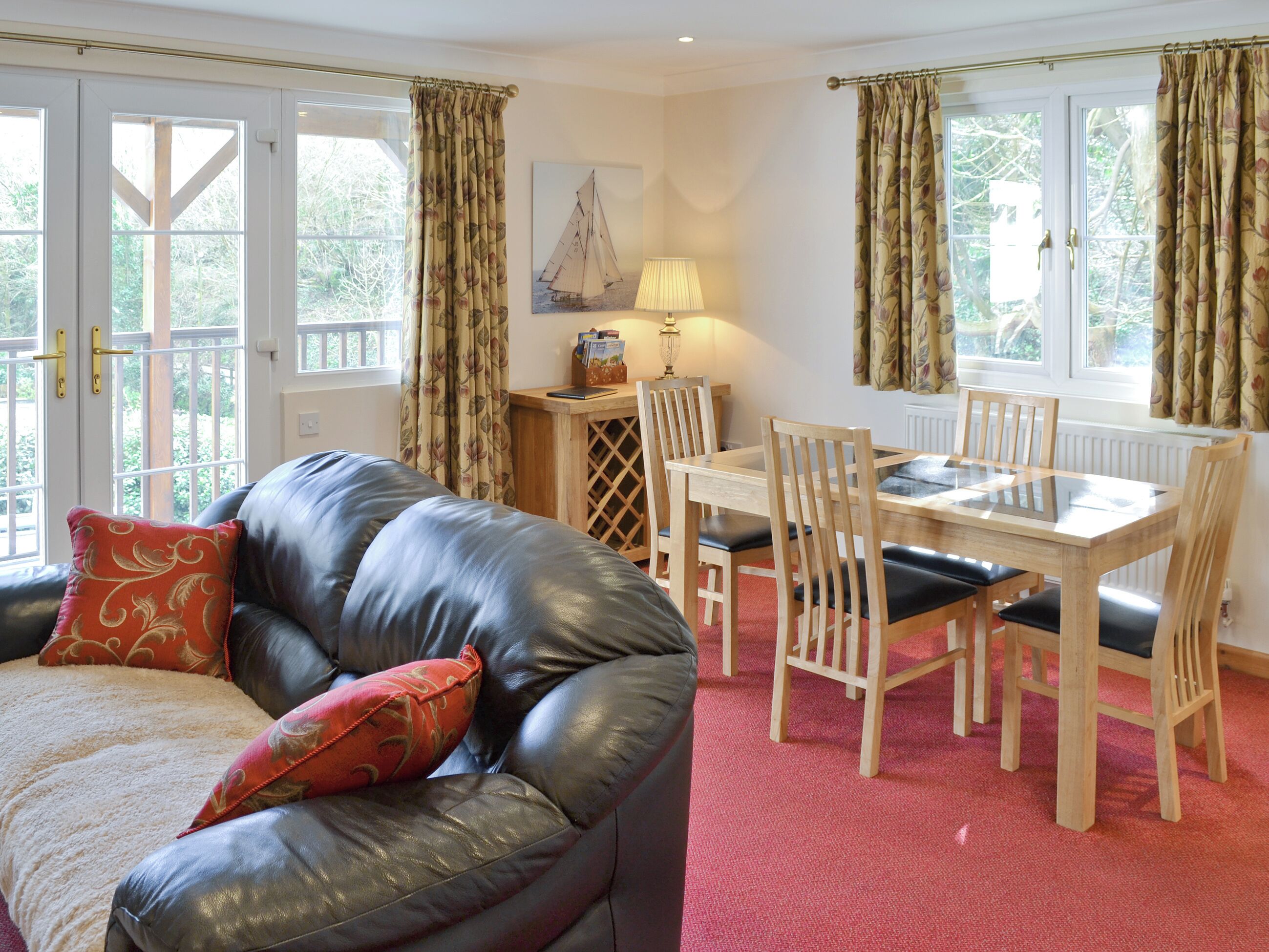 A cozy room with a leather sofa, a dining table with chairs, and a window with curtains.