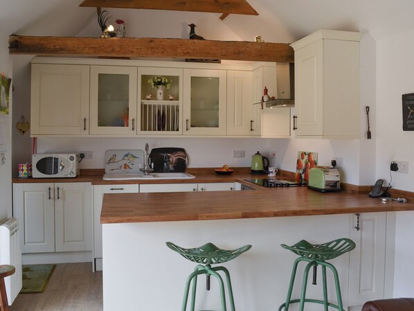 A kitchen with white cabinets, a wooden countertop, a microwave, a kettle, and two green bar stools. - 1 bedroom accommodation in Welton, near Lincoln (Welton, near Lincoln)