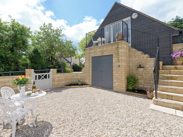 A house with a stone wall, a grey door, and a balcony with potted plants. - 1 bedroom accommodation in Mickleton, near Chipping Campden (Mickleton, near Chipping Campden)